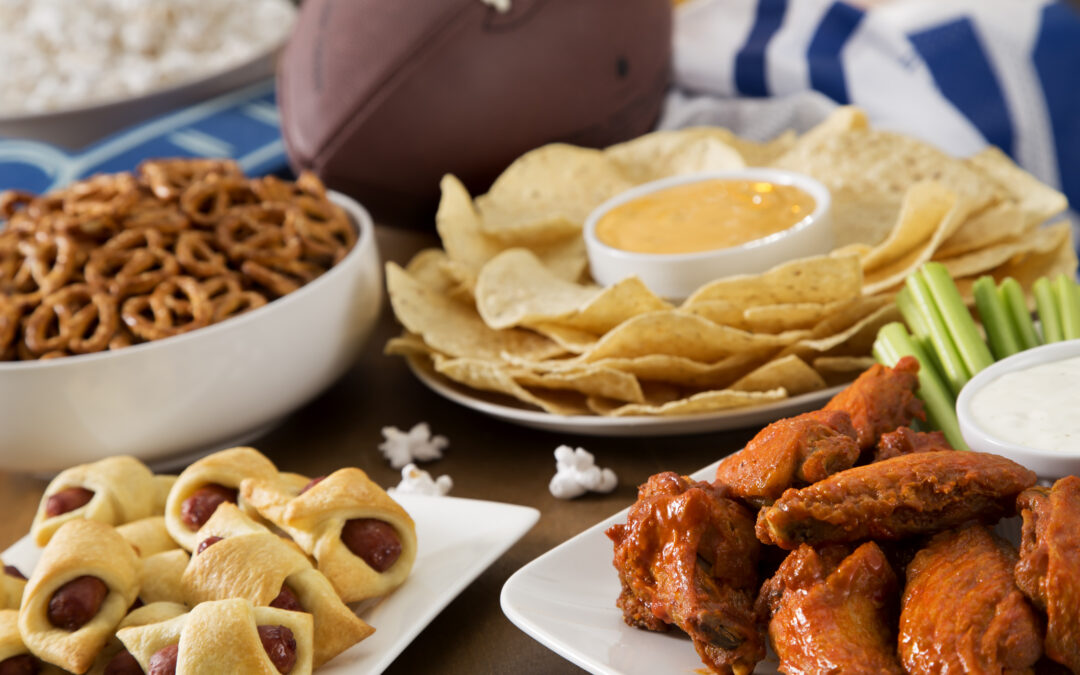 an assortment of tailgate party food, including wings, pigs in a blanket, pretxels, and nachos